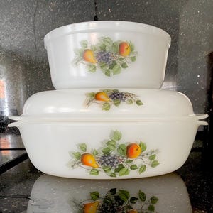 Puede incluir: Dos fuentes blancas para hornear apiladas una encima de la otra. Cada fuente presenta un diseño de frutas con peras, uvas y melocotones. Las fuentes están hechas de un material duradero y son perfectas para servir.