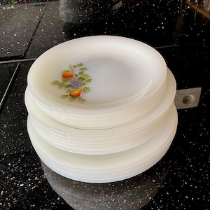 Puede incluir: Una pila de platos blancos y redondos con un diseño de frutas. Los platos tienen un diseño simple y elegante, con un patrón de frutas y flores en el centro. Los platos están apilados ordenadamente.