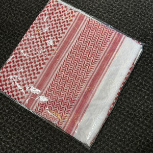 May include: A white and red patterned headscarf with a geometric design. The scarf is folded and packaged in a clear plastic bag.
