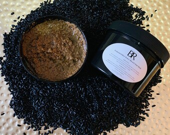 Könnte beinhalten: Ein schwarzer Plastikbehälter mit einem weißen Etikett, auf dem "Fermented Rice Water Miracle Hair Mask" steht, und einem schwarz-weißen Logo mit der Aufschrift "BR". Der Behälter ist mit einer braunen Haarmaske gefüllt und steht auf einem Bett aus schwarzem Reis.