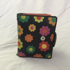 May include: Black bi-fold wallet with a colorful floral pattern. The flowers are in shades of green, yellow, orange, and pink. The wallet has a snap closure and an orange interior.