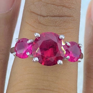 May include: A silver ring with three large, round, pink gemstones. The ring is worn on a finger.