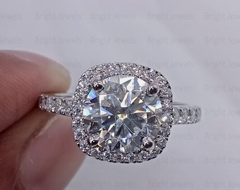 May include: A silver engagement ring with a large, round, clear diamond center stone. The diamond is surrounded by a double halo of smaller diamonds. The ring band is also set with smaller diamonds.