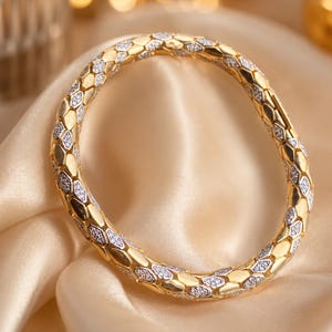 May include: A circular gold bangle bracelet featuring a repeating geometric pattern of smooth, polished gold hexagonal segments alternating with smaller, textured silver-toned segments encrusted with tiny, clear, sparkling stones.