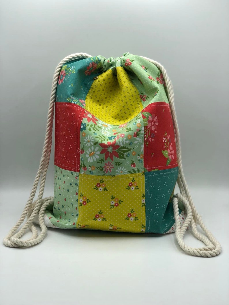 May include: A patchwork drawstring bag with a floral pattern in shades of green, yellow, red, and white. The bag has a white cotton rope drawstring.