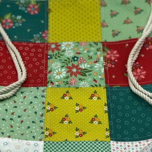 May include: A patchwork drawstring bag featuring a variety of floral patterns in shades of green, yellow, and red. The bag is made from cotton fabric and has a white drawstring.