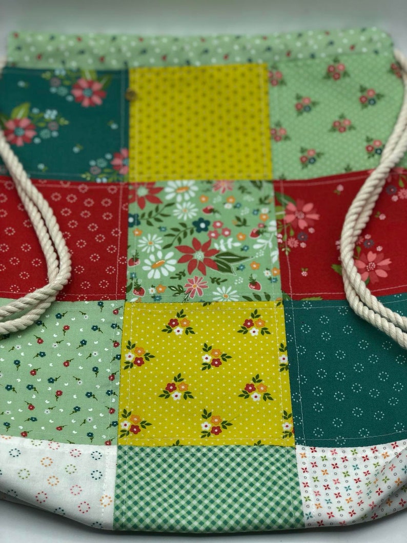 May include: A patchwork drawstring bag featuring a variety of floral patterns in shades of green, yellow, and red. The bag is made from cotton fabric and has a white drawstring.