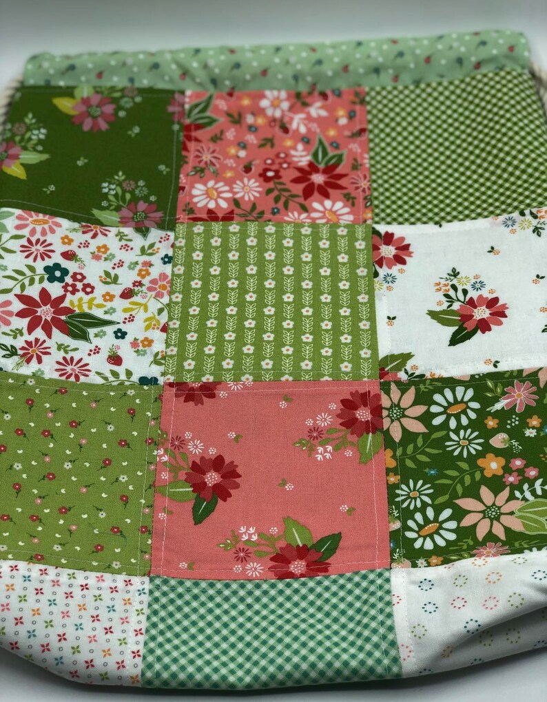 May include: A green and pink patchwork drawstring bag with a floral pattern. The bag is made of fabric and has a drawstring closure.