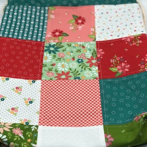 K&ouml;nnte beinhalten: Eine Patchwork-Kordeltasche mit verschiedenen floralen und geometrischen Mustern in Rot-, Gr&uuml;n- und Rosat&ouml;nen.