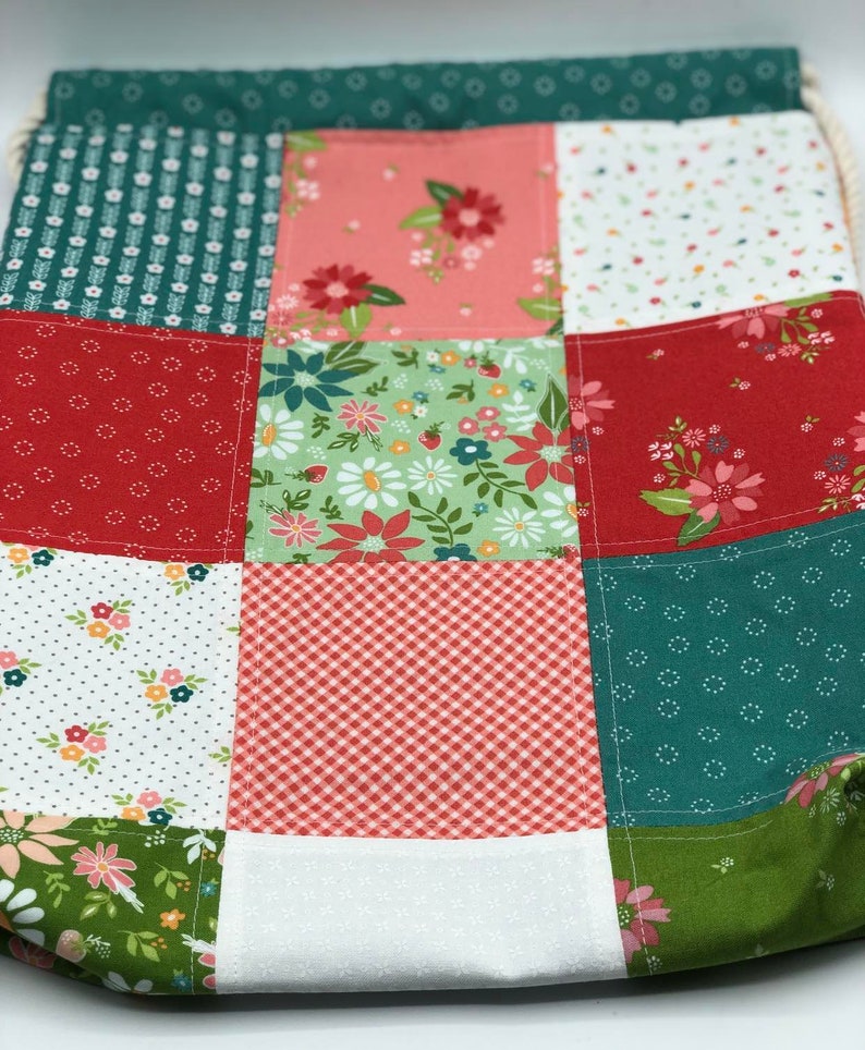 K&ouml;nnte beinhalten: Eine Patchwork-Kordeltasche mit verschiedenen floralen und geometrischen Mustern in Rot-, Gr&uuml;n- und Rosat&ouml;nen.