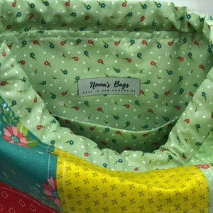 May include: A green fabric bag with a patchwork design. The bag has a drawstring closure and a label that reads "Nonna's Bags Made in New Hampshire".