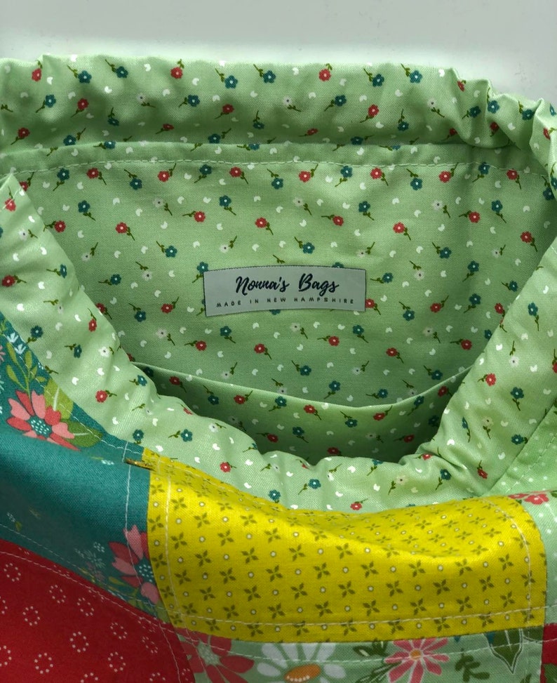 May include: A green fabric bag with a patchwork design. The bag has a drawstring closure and a label that reads "Nonna's Bags Made in New Hampshire".