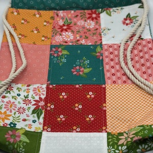 K&ouml;nnte beinhalten: Eine Patchwork-Kordeltasche mit verschiedenen Blumenmustern in Rot-, Orange-, Gr&uuml;n-, Rosa- und Wei&szlig;t&ouml;nen.