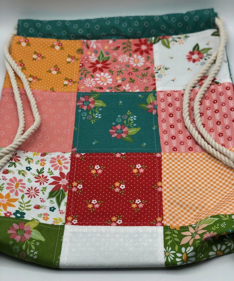 K&ouml;nnte beinhalten: Eine Patchwork-Kordeltasche mit verschiedenen Blumenmustern in Rot-, Orange-, Gr&uuml;n-, Rosa- und Wei&szlig;t&ouml;nen.