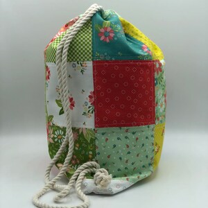 May include: A patchwork drawstring bag with a white rope handle. The bag is made of different fabrics with floral patterns in shades of red, green, yellow, and white.