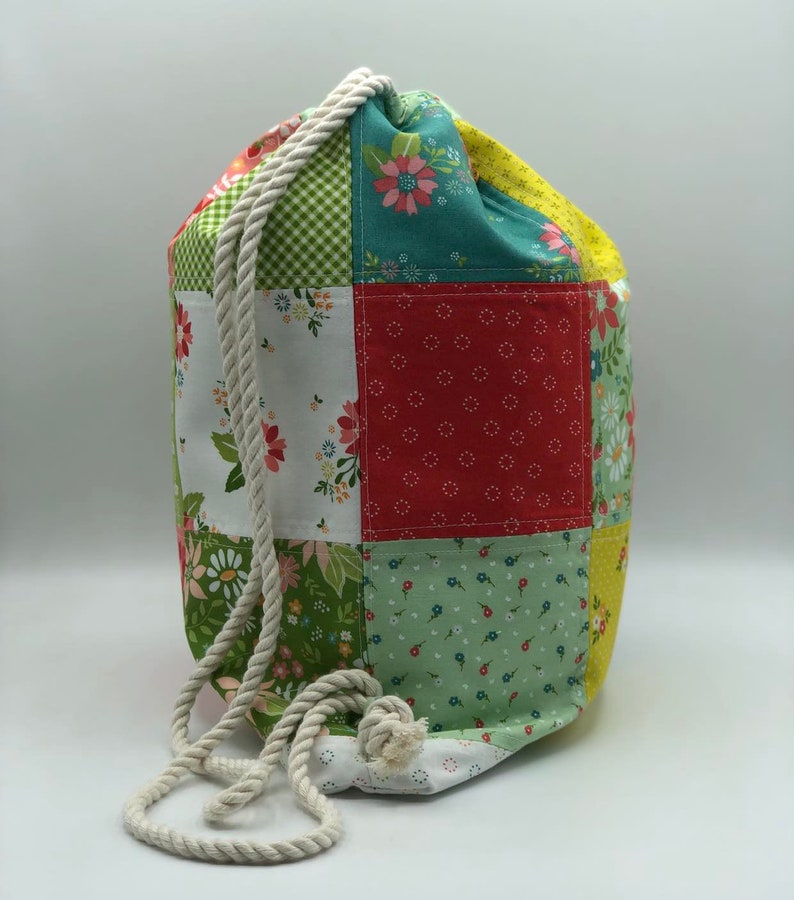 May include: A patchwork drawstring bag with a white rope handle. The bag is made of different fabrics with floral patterns in shades of red, green, yellow, and white.