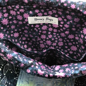 May include: Interior view of a fabric bag with a floral pattern. The lining features a dark blue background with pink star-shaped flowers. The bag has pockets and a label that reads "Nonna's Bags Made in New Hampshire."
