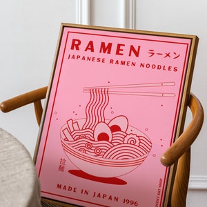 May include: A pink framed poster with a red illustration of a bowl of ramen noodles. The poster says "Ramen ラーメン Japanese Ramen Noodles Made in Japan 1996" and "Lucent Art Shop".