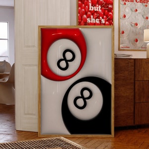 May include: A framed art print featuring a red and black eight ball design. The artwork is displayed on a white background, with a wooden frame. Two other framed prints are visible in the background, one with cherries and text, and another with cherries and text.