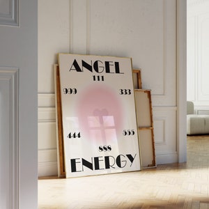May include: A white poster with a gold frame featuring the text "ANGEL 111 999 444 888 555 333 ENERGY" in black lettering. The poster has a pink heart shape in the center.