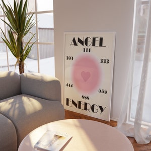 May include: A white framed poster with the words "ANGEL ENERGY" in black text. The poster has a pink gradient circle with a pink heart in the center and numbers around the circle: 999, 111, 333, 444, 888, 555.
