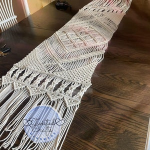 Könnte beinhalten: Cremefarbener Makramee-Tischläufer mit geometrischen Rauten- und Chevron-Mustern. Der Läufer hat einen Fransenrand und ist handgefertigt. Der Text "Twisted Crafts Handmade" ist unten links sichtbar.