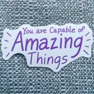 May include: A white sticker with the phrase "You are Capable of Amazing Things" in purple script. The sticker has a unique shape with dashed lines radiating from the edges, creating a visual accent.
