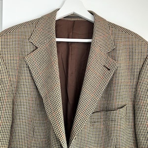 May include: A brown, black, and white houndstooth patterned blazer with a brown lining.