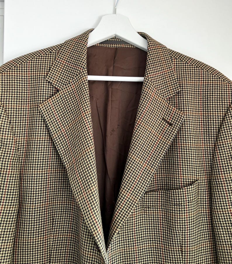 May include: A brown, black, and white houndstooth patterned blazer with a brown lining.