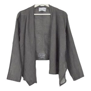 May include: A gray linen cardigan with a draped front and long sleeves. The cardigan has a white label with the text "remarkable" on it.