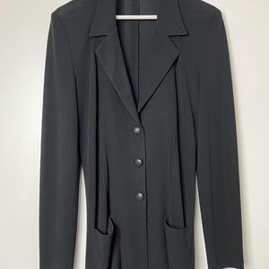 May include: A black blazer with a long sleeve, four buttons, and two pockets. The blazer has a label that says "T.Y. Collection" in red.