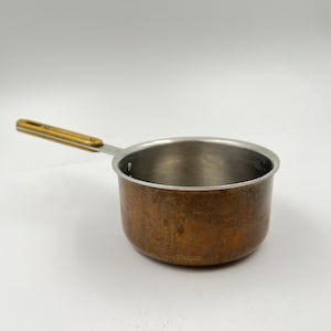 Puede incluir: Una pequeña cacerola de cobre con un mango de latón. La cacerola tiene un interior de acero inoxidable.