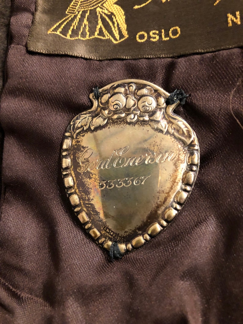 May include: Silver-toned metal tag with a heart-shaped design and a floral border. The tag has the text "God Bless" and the number "533367" engraved on it.