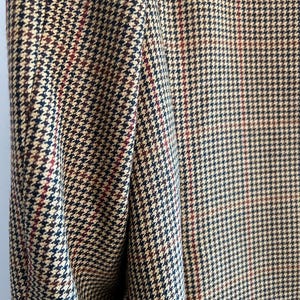 May include: Close-up of a brown, black, and red houndstooth patterned fabric. The fabric has a subtle sheen and a textured weave.