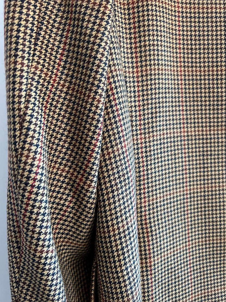May include: Close-up of a brown, black, and red houndstooth patterned fabric. The fabric has a subtle sheen and a textured weave.