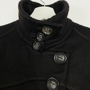 Może przedstawiać: Zbliżenie na kołnierz i guziki czarnego płaszcza. Guziki mają wygrawerowane słowo "VERSACE".