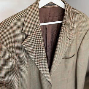 May include: A brown, black, and red plaid blazer with a brown lining. The blazer has a single button closure and two pockets.