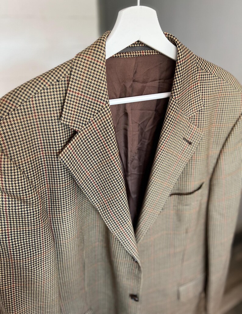 May include: A brown, black, and red plaid blazer with a brown lining. The blazer has a single button closure and two pockets.