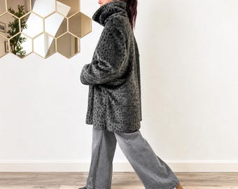 May include: A dark gray faux fur coat featuring a subtle black leopard print pattern, a high collar, and long sleeves. The coat is paired with wide-leg gray denim jeans and black shoes, creating a layered look with a textured, soft-touch finish.