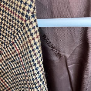 May include: Close-up of the brown lining of a blazer with a brown, black, and beige houndstooth pattern. The lining has the word "Realization" embroidered on it.