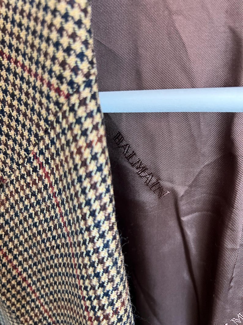 May include: Close-up of the brown lining of a blazer with a brown, black, and beige houndstooth pattern. The lining has the word "Realization" embroidered on it.