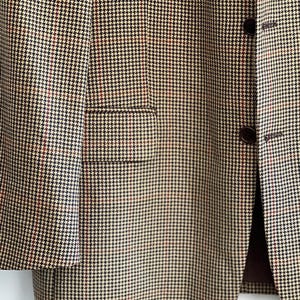 May include: A brown and beige blazer with a houndstooth pattern. The blazer has a single button closure and a flap pocket on the left side.
