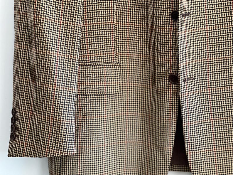 May include: A brown and beige blazer with a houndstooth pattern. The blazer has a single button closure and a flap pocket on the left side.