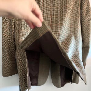 May include: A brown and tan plaid blazer with a brown lining. The blazer is unbuttoned and the lining is visible.