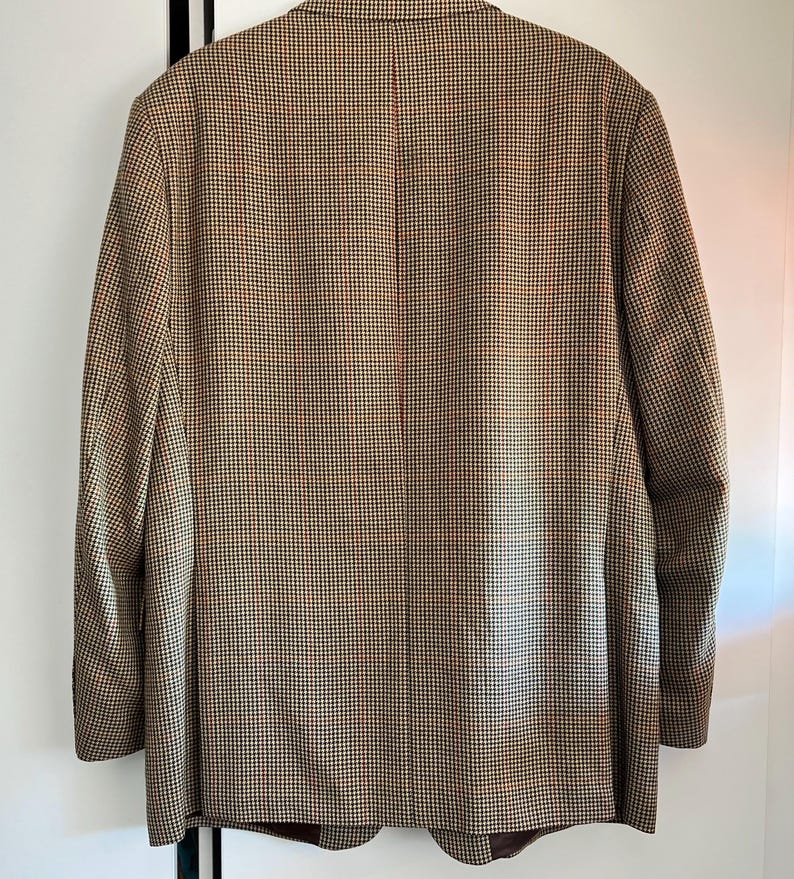 May include: A brown, black, and white patterned blazer. The blazer has a single button closure and a notched lapel.