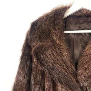May include: A brown fur coat with a large collar. The coat is hanging on a white hanger.