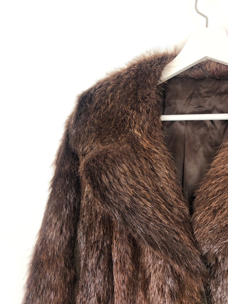 May include: A brown fur coat with a large collar. The coat is hanging on a white hanger.
