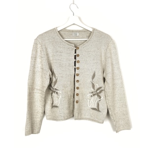May include: A beige cardigan with a round neckline and a button-up front. The cardigan has embroidered floral designs on the front and is made of a soft, textured fabric.
