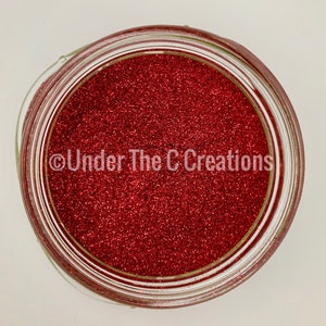 May include: A glass jar filled with red glitter. The jar has a clear lid and the glitter is a fine, sparkly texture. The text "Under The C Creations" is printed on the jar.