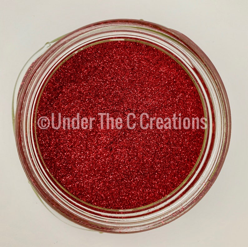 May include: A glass jar filled with red glitter. The jar has a clear lid and the glitter is a fine, sparkly texture. The text "Under The C Creations" is printed on the jar.